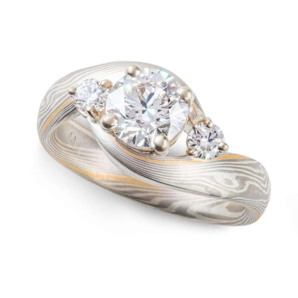 mokume gane wedding ring, band is twisted around the setting in the center, three diamonds, a larger one in the center with two smaller side stones.