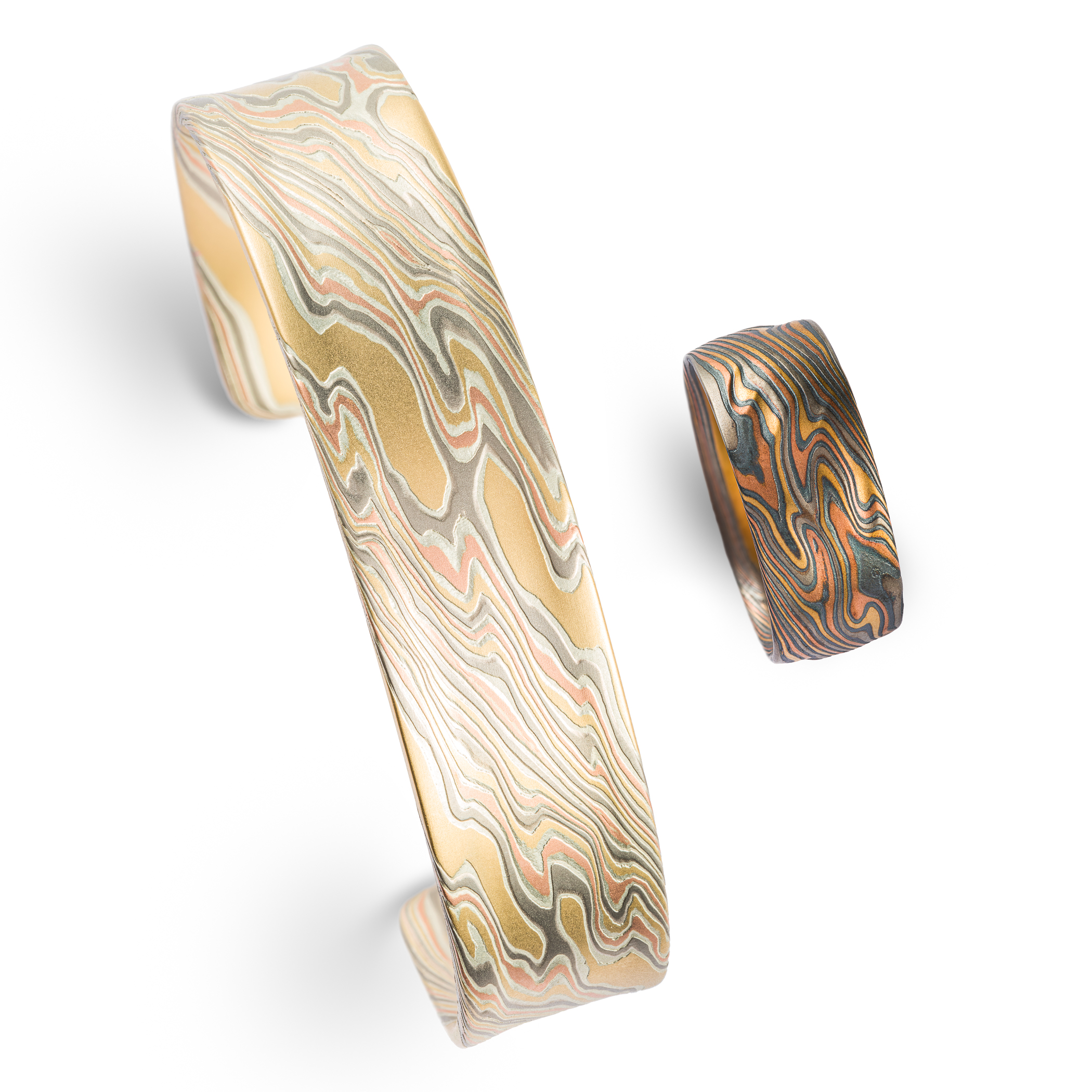 Mokume gane patterned bracelet and ring sitting side by side on a white background, made with a mixture of red and yellow gold, palladium and silver.