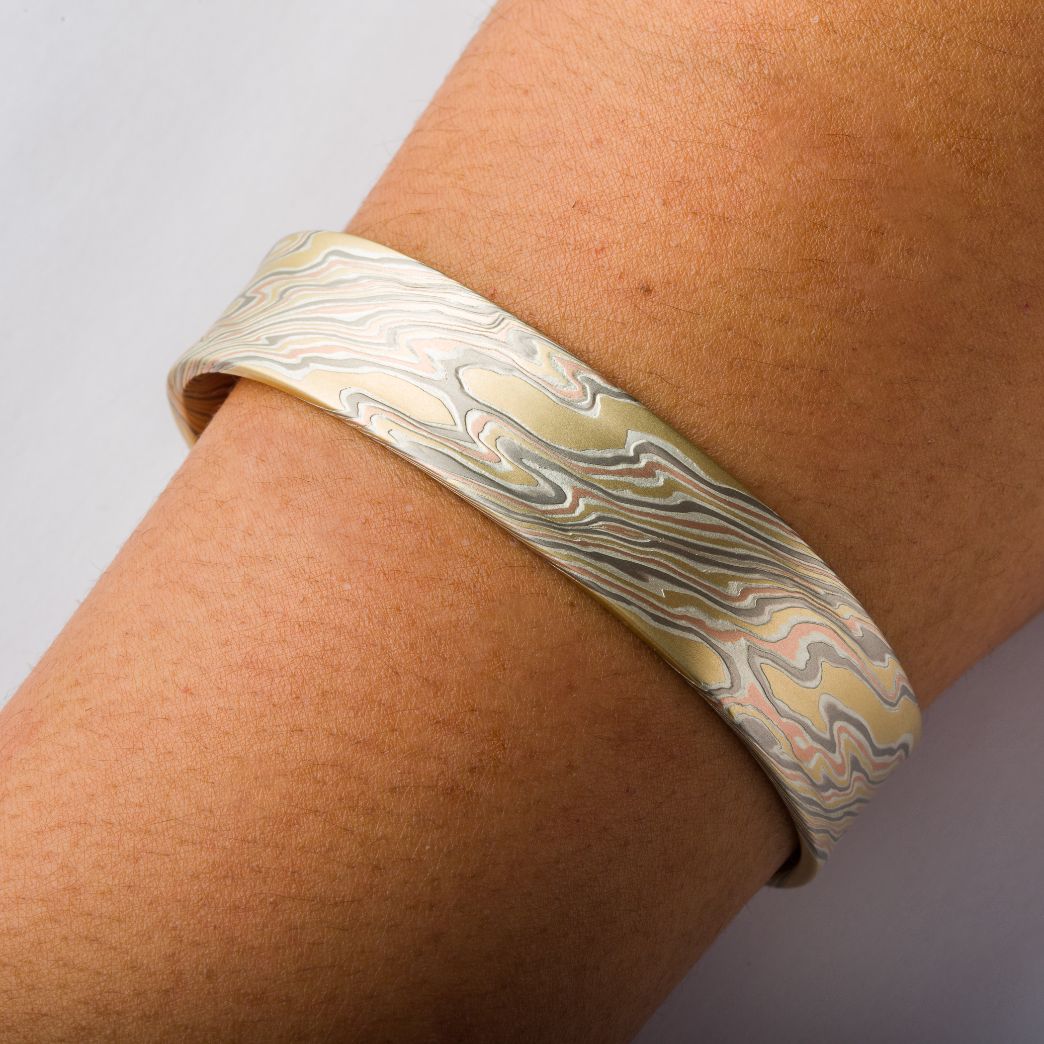 Mokume gane patterned mens bangle, wide, slightly textured, made with yellow gold, red gold, palladium and silver.