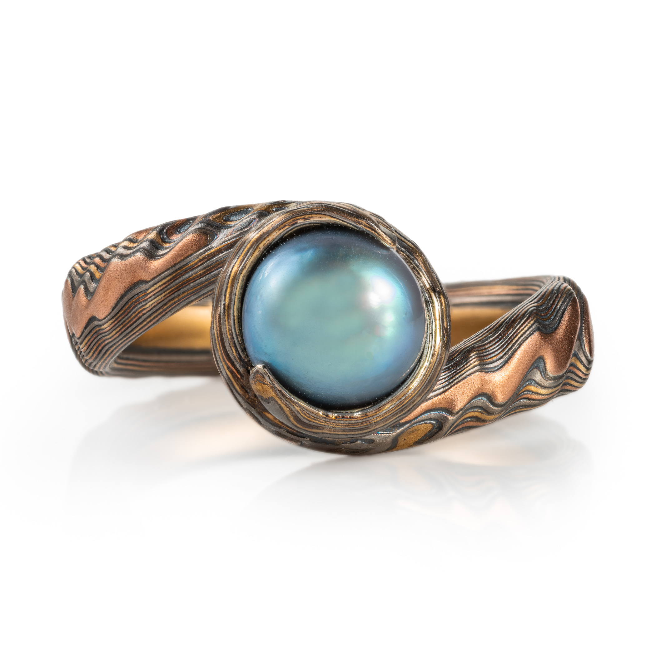 custom blue pearl in a swirled of bypass setting with woodgrain metal all around the pearl holding it in a circle