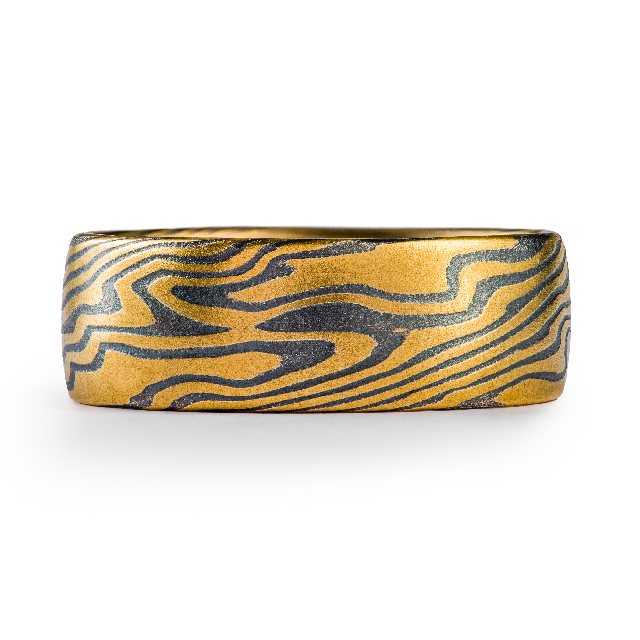 Wide men's style mokume gane ring made with layers of yellow gold and oxidized silver (black), in a dynamic twisting pattern.