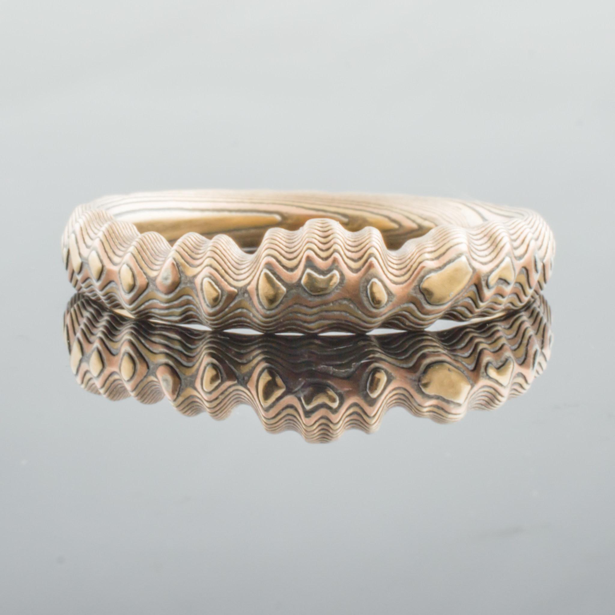 Uniquely contoured mokume gane ring with a shaped edge made to fit with an engagement ring, and textured to look like topography.