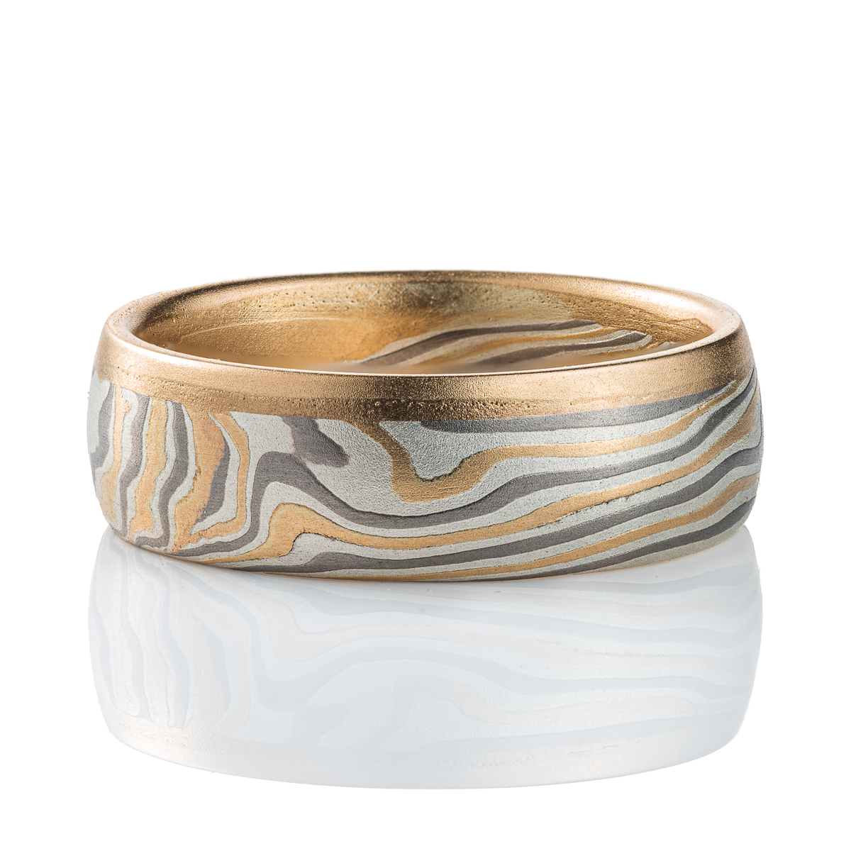 Mokume gane ring made of twisting layers of oxidized silver, palladium and yellow gold, with a solid strip of yellow gold running around one edge.